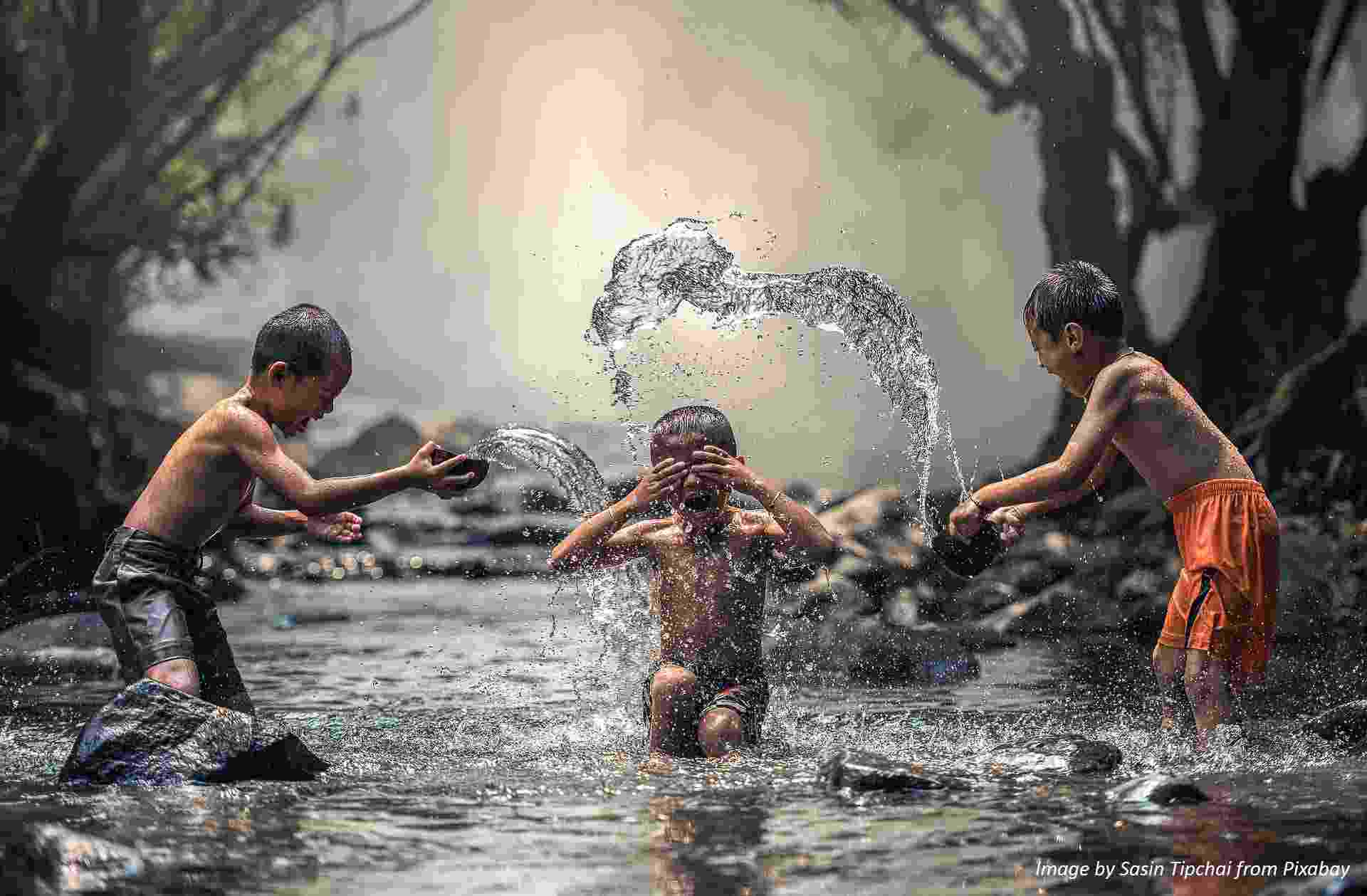 Three young boys joyfully throw water over each other playing in a river